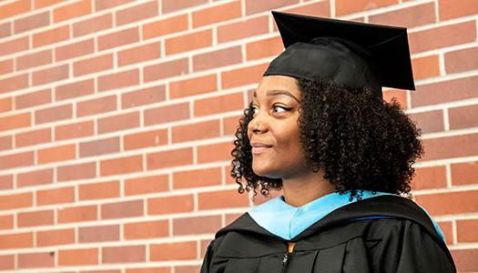 a woman wearing a graduation cap and gown stands in front of a brick wall